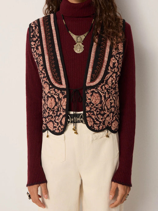 Person wearing a burgundy sweater, patterned vest, and white pants on a plain background, luna vest Maison hotel aprilmae chiswick 